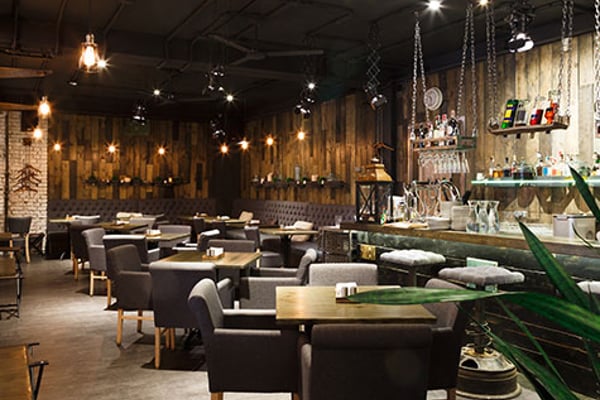 Modern bar and lounge with dark leather seating, wooden accent walls, hanging pendant lights, and shelves of bottles behind the counter.