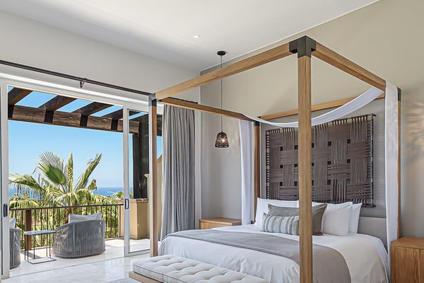 Luxury bedroom with wooden canopy bed, ocean view through glass doors, and palm trees on terrace